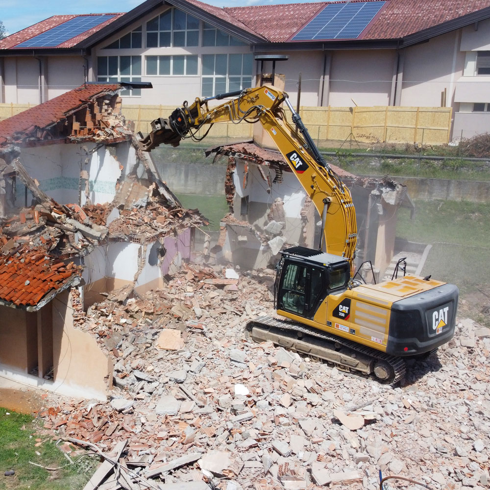 Escavatore al lavoro in un cantiere di demolizione, foto frontale mentre l'escavatore cingolato demolisce un edificio