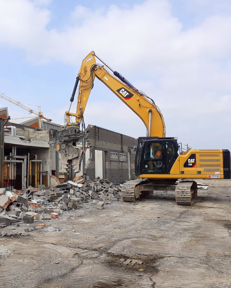 Mezzo escavatore idraulico Caterpillar 330 cingolato in un cantiere mentre demolisce un edificio industriale